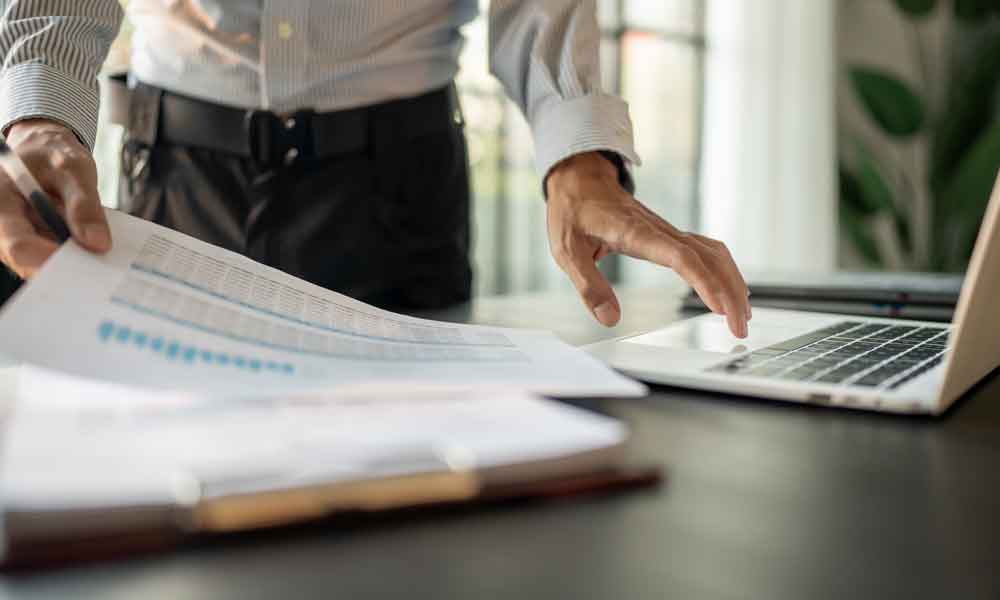 Accountant analyzing investment charts and pressing calculator buttons over documents.