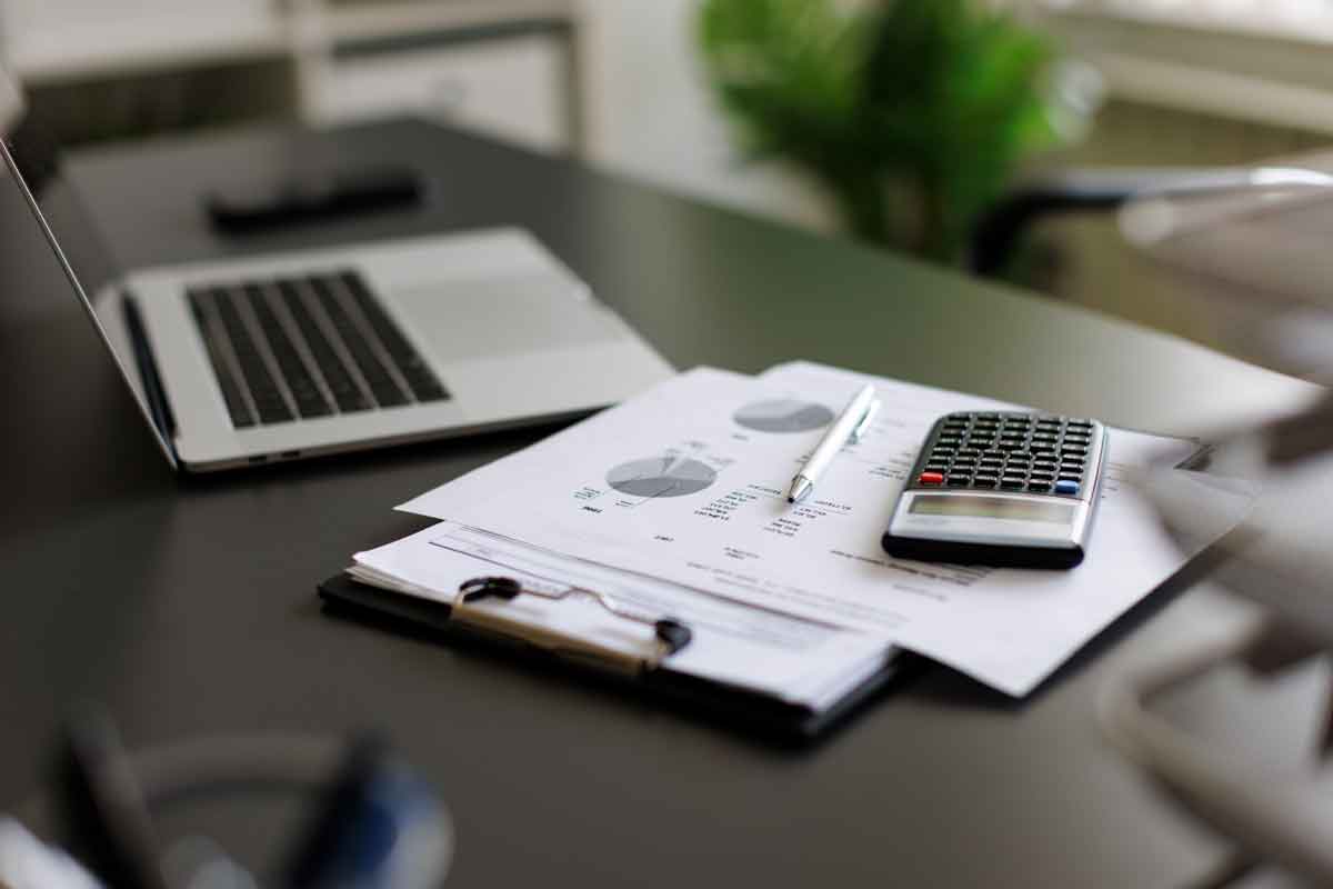 Work desk with a laptop, paperwork and a calculator on it.